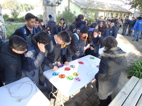 Un grupo de estudiantes está participando en una actividad al aire libre, interactuando con objetos coloridos sobre mesas.