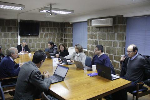 Reunión en una sala con varias personas sentadas alrededor de una mesa con laptops.