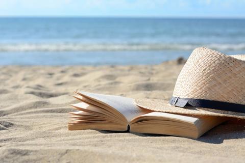 Un sombrero de paja y un libro descansando en la arena de la playa.