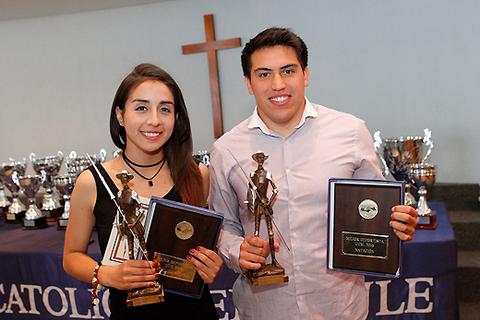Dos jóvenes sonrientes sostienen premios en un evento de reconocimiento académico.