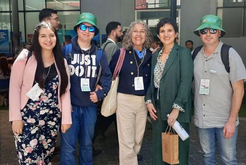 Un grupo de cinco personas sonríen en un evento al aire libre, vistiendo camisetas y gorras.