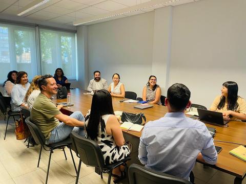 Un grupo de personas se encuentra reunido en una sala de juntas, conversando y trabajando en equipo.