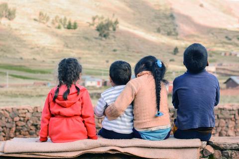 Un grupo de niños está sentado mirando hacia un paisaje montañoso.