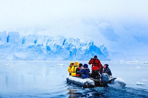Un grupo de personas en una embarcación inflable navega cerca de un glaciar en un paisaje nevado.