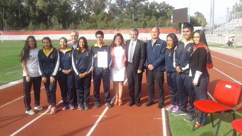 Grupo de estudiantes y autoridades en una ceremonia en un campo deportivo.