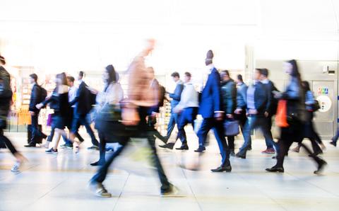 Una multitud de personas caminando rápidamente en un entorno urbano concurrido.