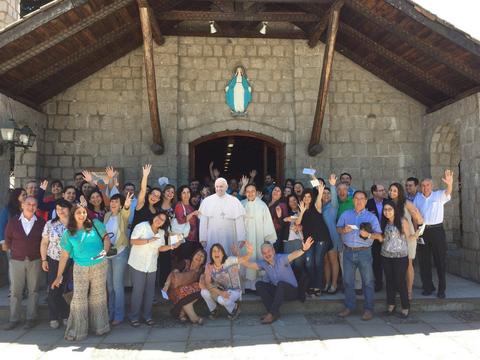 Un grupo de personas sonrientes y levantando las manos frente a una iglesia.
