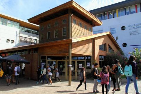 Edificio de estilo moderno con un diseño de madera, rodeado de estudiantes en un ambiente escolar.