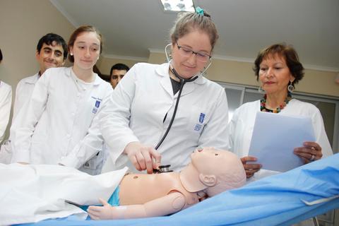 Un grupo de estudiantes observa mientras una estudiante utiliza un estetoscopio en un maniquí educativo.