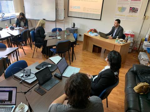 Una reunión en una sala de conferencias con varias personas sentadas en mesas y un presentador al frente.