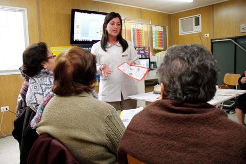 Una profesional de la salud presenta información a un grupo de personas mayores en una reunión.