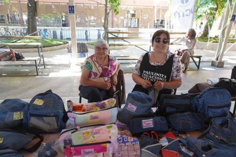 Dos mujeres sonríen mientras muestran sus productos hechos a mano en un mercado al aire libre.