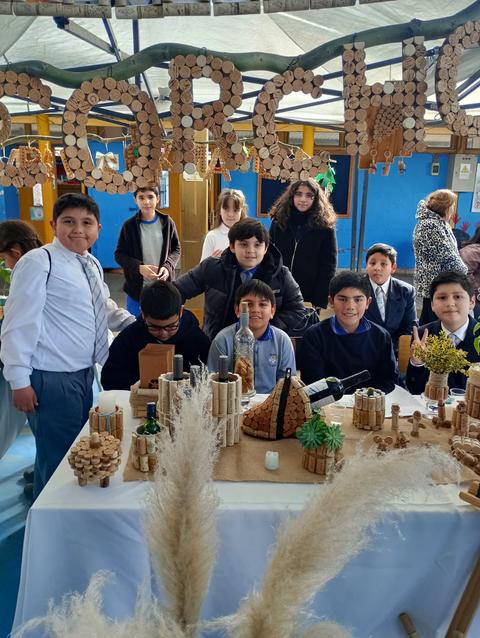 Un grupo de niños y adolescentes sonríen en una exposición de proyectos que incluyen decoraciones de corcho.