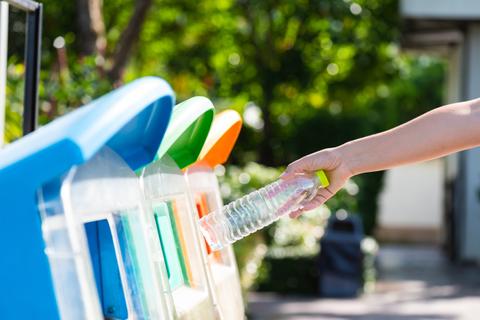 Una persona está depositando una botella de plástico en un contenedor de reciclaje.