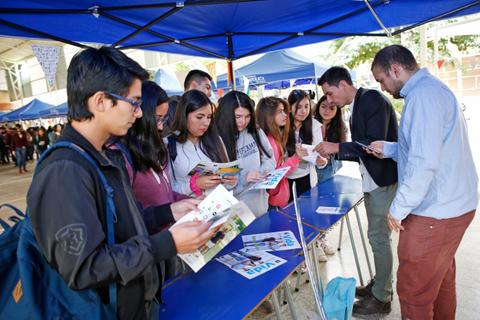 Un grupo de estudiantes observan material informativo en un evento al aire libre.