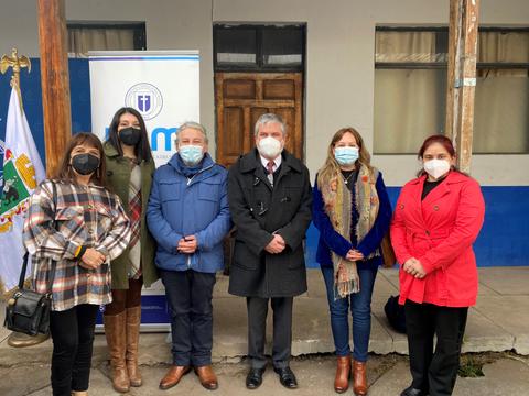 Un grupo de seis personas posando juntas en un evento al aire libre, con banderas y un cartel detrás.