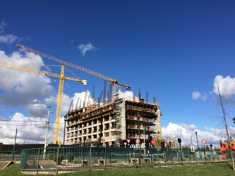 Un edificio en construcción rodeado de grúas y señales de tráfico bajo un cielo azul.
