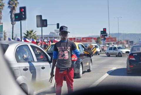 Un joven vendedor ambulante se encuentra en una intersección vial ofreciendo productos a los conductores.