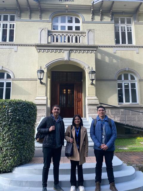 Tres personas posando frente a un edificio con un diseño arquitectónico clásico.
