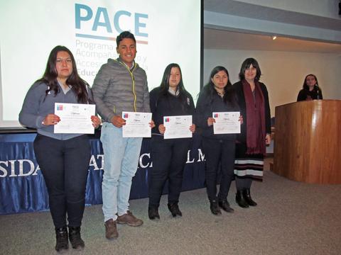 Un grupo de estudiantes sostiene certificados durante un evento de entrega en una sala de conferencias.