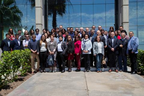 Un grupo de personas sonrientes posando juntas frente a un edificio moderno con ventanas reflejantes.