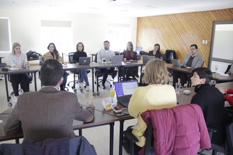Una reunión de trabajo en un ambiente colaborativo donde varias personas están sentadas alrededor de una mesa con computadoras portátiles.