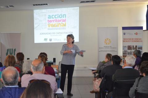 Una mujer presenta un taller sobre acción territorial en un evento de capacitación con asistentes en un salón.