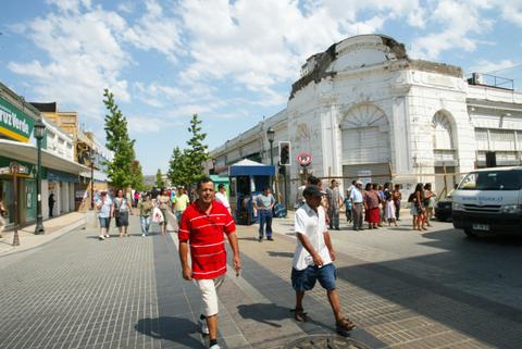 Una escena bulliciosa en una calle, con personas caminando y tiendas a los lados.