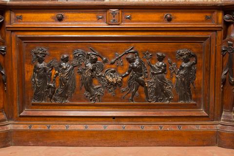 Relieve en bronce sobre un panel de madera que representa figuras humanas y elementos ornamentales.