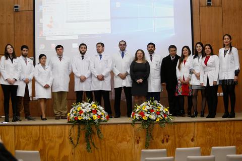 Un grupo de médicos y médicos en formación posa en un escenario con flores de fondo.