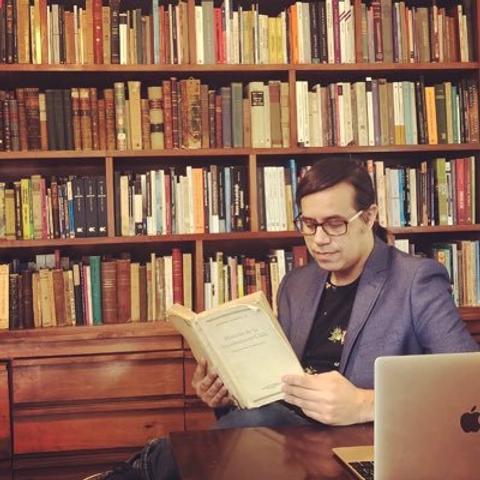 Un hombre está leyendo un libro en una biblioteca con estanterías llenas de libros.