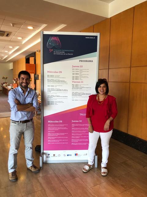 Dos personas posan junto a un cartel informativo sobre un evento.