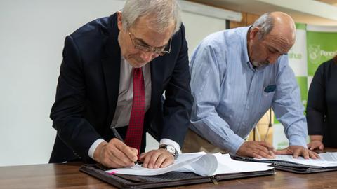 Dos personas firmando documentos en una mesa.