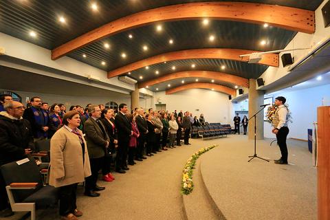 Un grupo de personas se encuentra de pie en un auditorio mientras una persona canta frente a un micrófono.