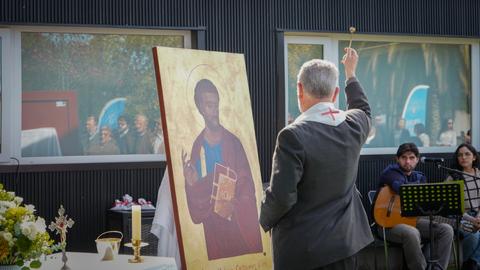 Un sacerdote realiza un ritual de bendición frente a una imagen religiosa en un evento al aire libre.