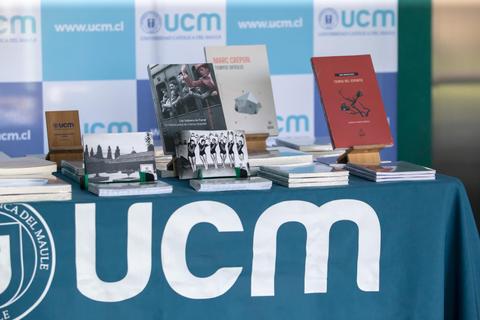 En la imagen se observa una mesa con libros expuestos y una tela con el logo de UCM.