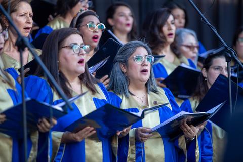 Un coro de mujeres canta con uniformes azules y dorados en un concierto.