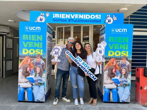 Un grupo de personas da la bienvenida a nuevos estudiantes frente a un cartel que promueve la universidad.
