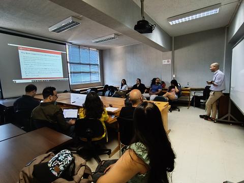 Una presentación en aula donde un grupo de personas escucha a un expositor frente a una pantalla.