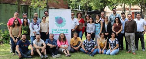 Un grupo diverso de personas sonríen frente a un cartel de Red Campus Sustentable en un entorno al aire libre.
