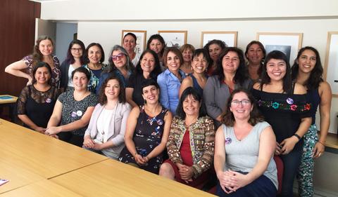 Un grupo de mujeres sonrientes posando juntas en una sala de reuniones.