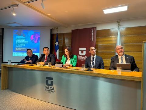 Un panel de discusión académico con varias personas sentadas detrás de un escritorio en un evento en la Universidad de Talca.