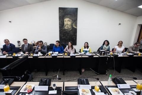 Una reunión en una sala con varias personas sentadas alrededor de una mesa y un retrato en la pared.