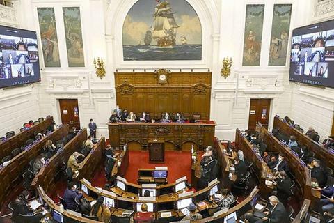 Vista del interior de un recinto legislativo con varios asistentes y pantallas en las paredes.