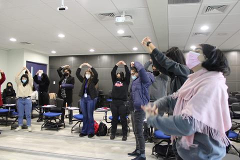 Un grupo de personas en un aula levantando las manos en un ejercicio grupal.