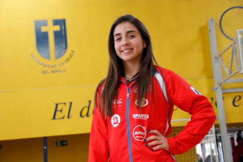 Una joven sonriente con un uniforme rojo posando en un gimnasio con paredes amarillas.
