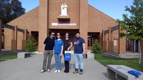 Un grupo de cuatro personas posa frente a un edificio con arquitectura moderna y un jardín bien cuidado.