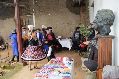 Una pareja baila en un ambiente festivo adornado con productos locales y amigos observando.