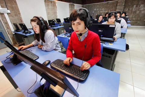 Un grupo de estudiantes en un aula de computación, concentrados en sus pantallas mientras usan auriculares.