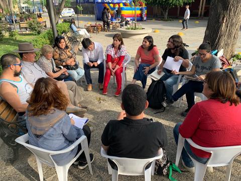 Un grupo de personas sentadas en círculo en un espacio al aire libre, participando en una conversación o actividad grupal.